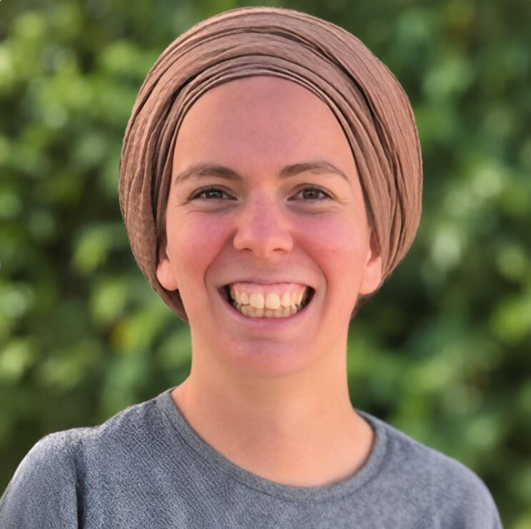 Portrait de Yemima Shindler. Life Coach. Portrait de Yemima, coach de vie, souriante et portant un turban beige sur fond de verdure.